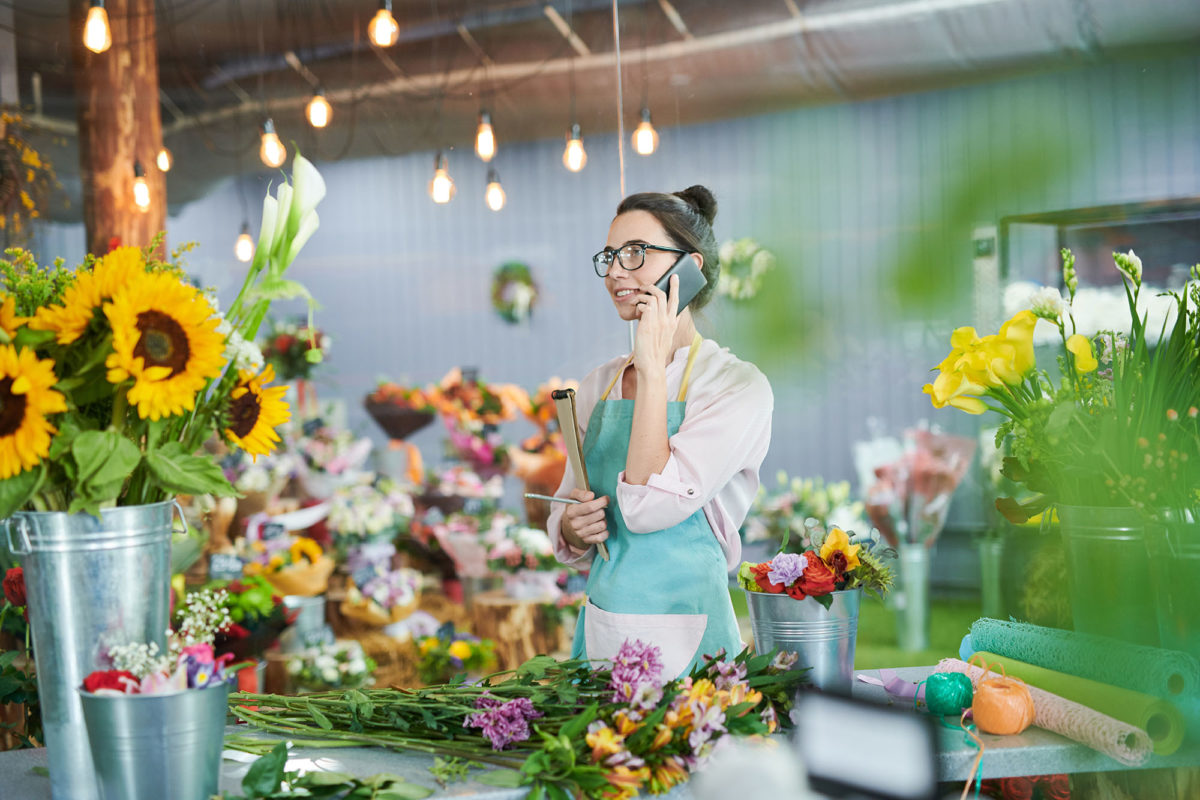 Side view portrait of young woman speaking by phone in flower shop